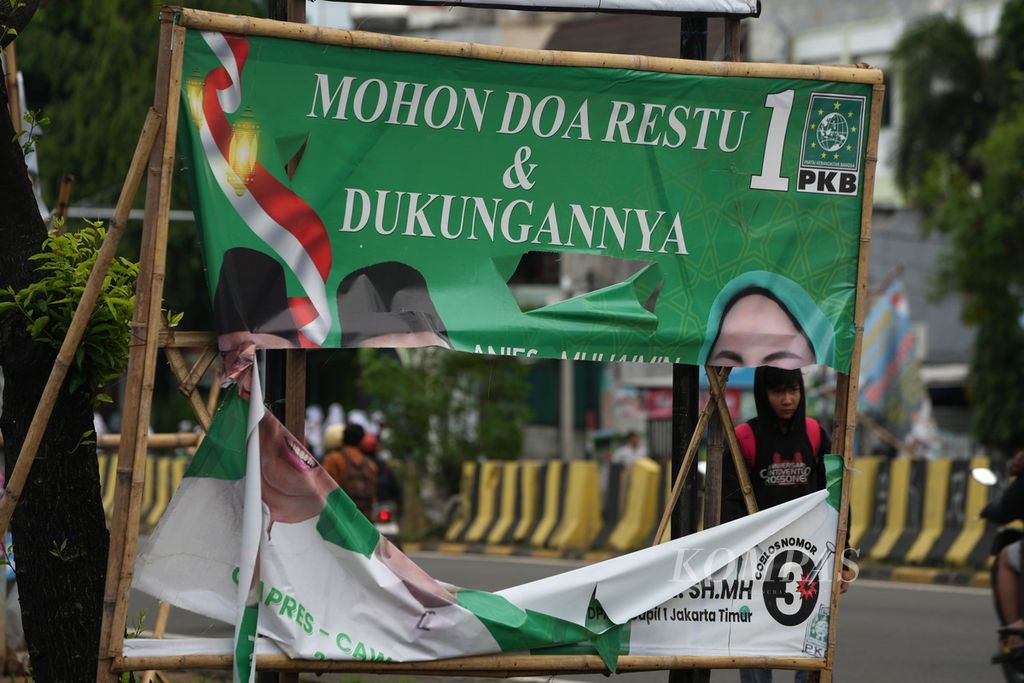 Warga melintasi baliho calon anggota legislatif yang sobek di Jalan Pahlawan Revolusi, Jakarta Timur, 19 Januari 2024. 