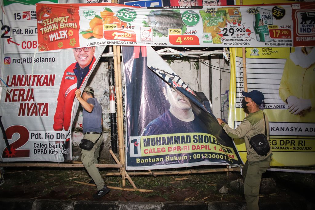 Petugas Satpol PP menurunkan alat peraga kampanye (APK) yang masih terpasang di Surabaya, Jawa Timur, Minggu (11/2/2024) dini hari. 