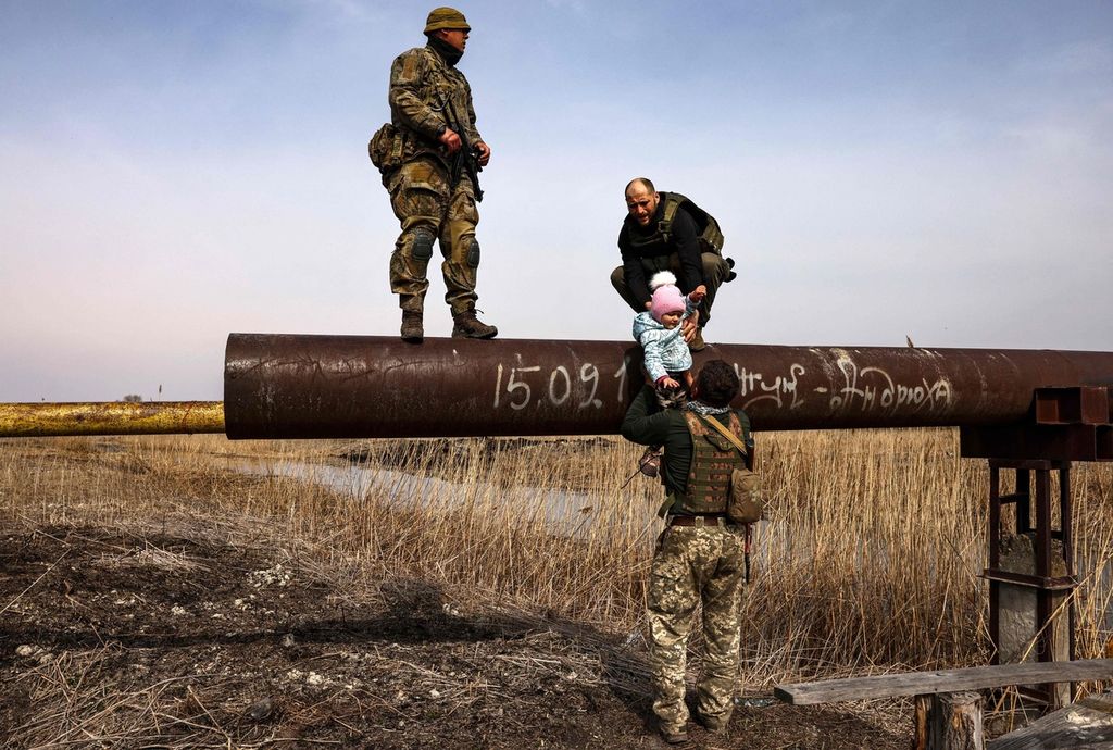Seorang tentara Ukraina, Andriy tengah mengulurkan seorang pengunsi anak kepada temannya, setelah ia membawanya menyeberangi sungai di pinggiran kota Kiev pada Kamis (31/3/2022).