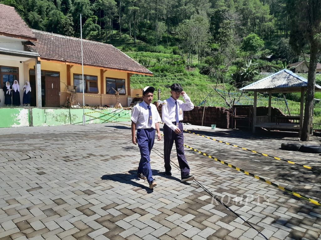 Dua siswa SMP Satu Atap berjalan di dekat lokasi retakan di halaman SD-SMP Satu Atap di Dusun Brau, Desa Gunungsari, Kecamatan Bumiaji, Kota Batu, Jawa Timur, Minggu (19/3/2024).