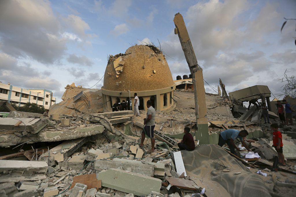 Beberapa warga berdiri di atas reruntuhan bangunan masjid yang rusak akibat serangan militer Israel ke Khan Younis, Jalur Gaza, MInggu (8/10/2023). 