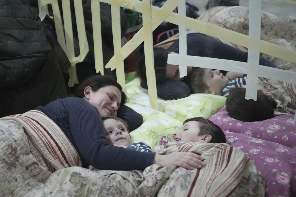 Seorang perempuan dan anak-anaknya berbaring di lantai di tempat pengungsian di Mariupol, Ukraina, 27 Februari 2022. 