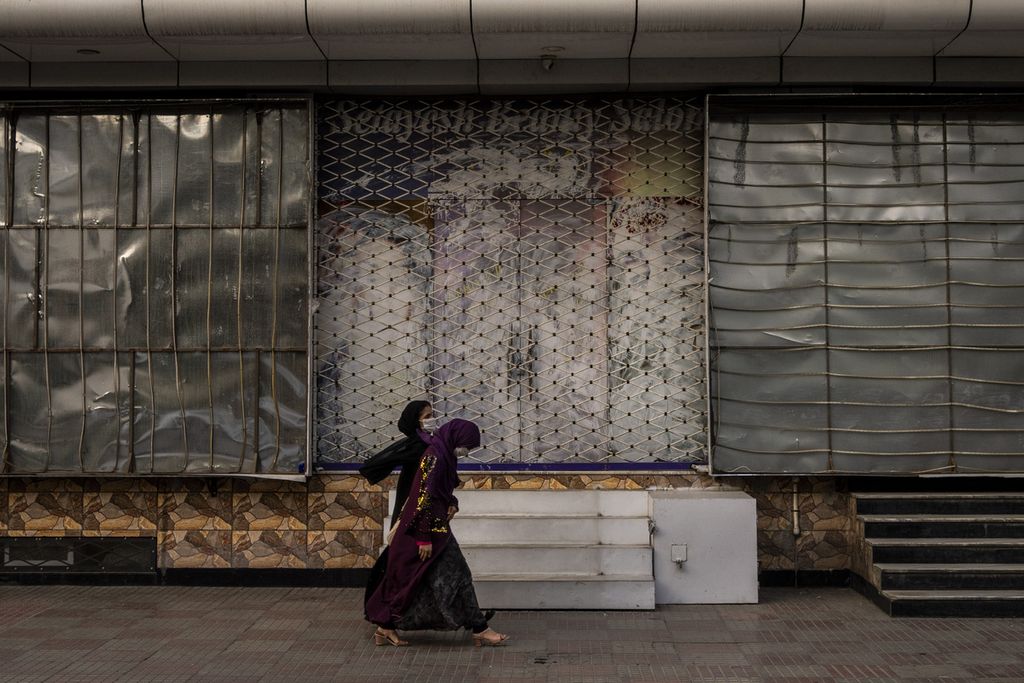 Perempuan Afghanistan berjalan melewati sebuah salon kecantikan yang tutup di Kabul,  11 September 2021. 
