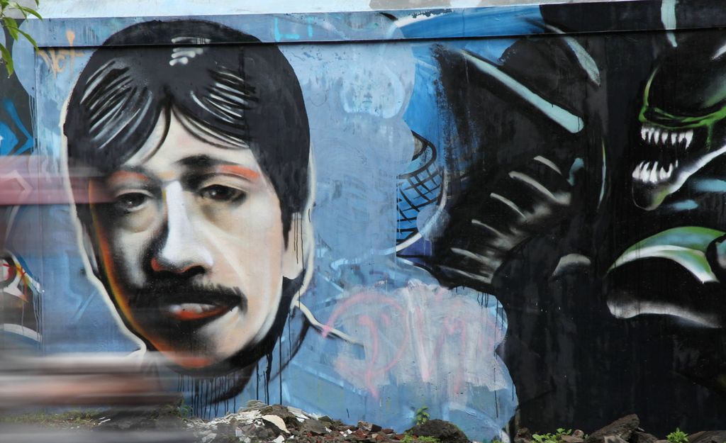 Warga melintas di depan mural yang melukiskan wajah Munir, pejuang hak asasi manusia, di kawasan Dinoyo, Kota Malang, Sabtu (22/2). Meskipun telah meninggal, perjuangan dan semangat Munir tetap dilanjutkan oleh para penerusnya.