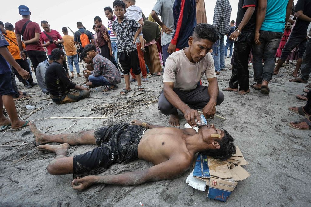 Seorang pria memberikan minum kepada pengungsi Rohingya yang tiba dengan berenang dari kapal yang mengangkutnya di Pineung, Provinsi Aceh, pada 16 November 2023. 
