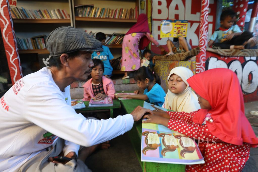 Ketua RT 004 sekaligus penggerak literasi, Naidih Muhammad Zein, menemani anak-anak membaca buku di Bale Buku di perkampungan Gang Dendrit, RT 004 RW 008, Kecamatan Cakung, Jakarta Timur, Jumat (12/5/2023). Tempat ini dibuat untuk menumbuhkan minat membaca bagi anak-anak. 