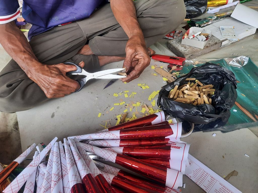 Rojali (50) memotong kertas yang akan diselipkan pada bambu sebagai alat yang membuat trompet kertas berbunyi di kawasan Kota Tua, Jakarta, Sabtu (31/12/2022). Trompetnya dijual seharga Rp 5.000 per buah.