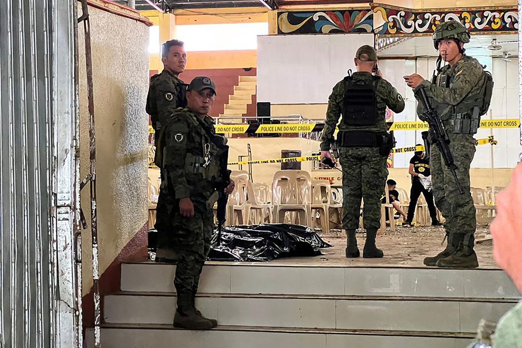 Personel militer berjaga di pintu masuk sasana saat penyelidik (di latar belakang) mencari bukti-bukti setelah ledakan bom di Universitas Negeri Mindanao di Marawi, Filipina, Minggu (3/12/2023). Ledakan itu terjadi saat misa, menewaskan empat orang dan melukai puluhan orang lainnya. 