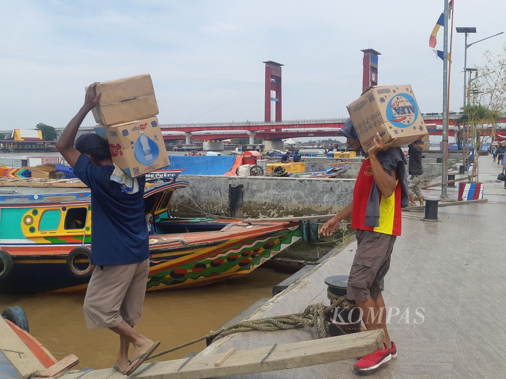 Dua buruh mengangkat barang ke kapal jukung di Pelabuhan 16 Ilir, Palembang, Sumatera Selatan, Sabtu (15/7/2023). Dua pelabuhan sungai di 7 Ulu dan 16 Ilir direnovasi. Kawasan ini menjadi poros ekonomi di Palembang.