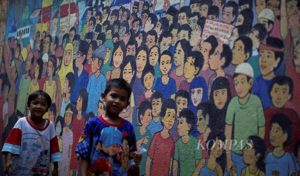 Anak-anak melintas di depan mural yang menghiasi tembok-tembok kampung di Kebon Baru, Tebet, Jakarta Selatan, Rabu (19/4). Mural bertema keberagaman dan kebinekaan terus digemakan untuk persatuan dan kesatuan rakyat.