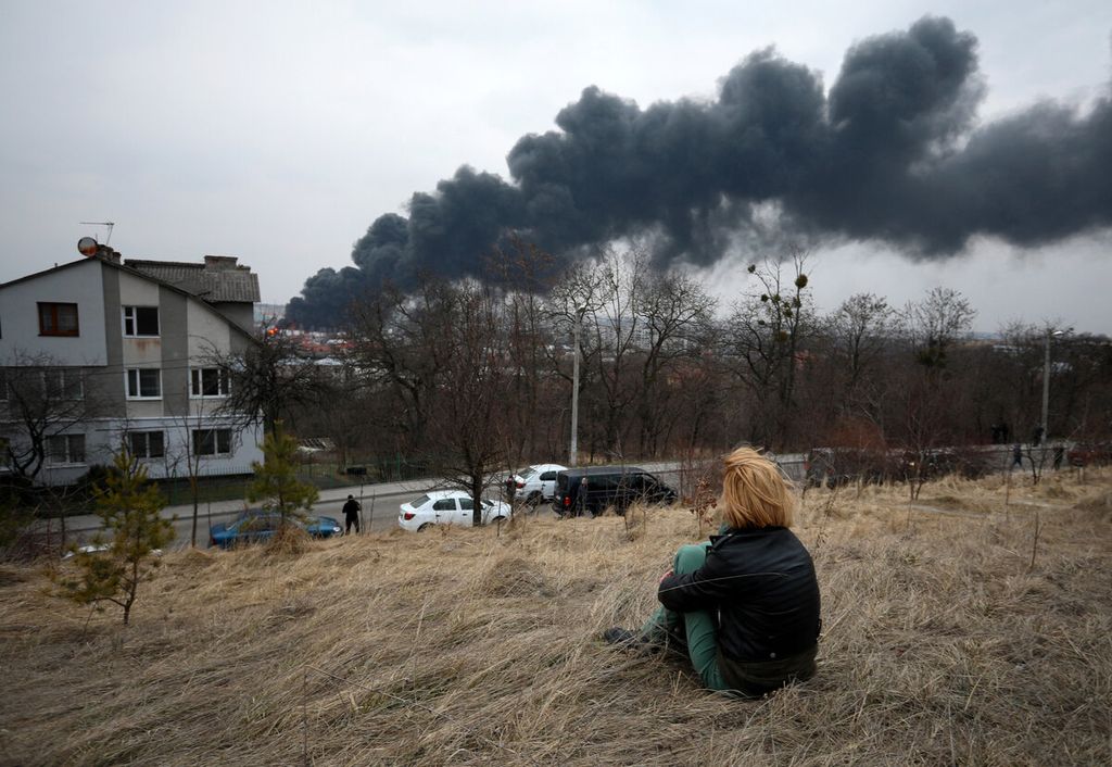 Seorang perempuan melihat asap hitam yang ditimbulkan dari serangan udara militer Rusia di Kota Lviv, Ukraina, Sabtu (26/3/2022). Serangan udara itu menyebabkan lima orang terluka. Dalam sebulan ini, militer Rusia telah menyerang sejumlah kota di Ukraina.