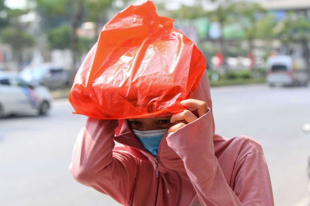 Foto yang diambil pada 22 Mei 2023 ini memperlihatkan seorang perempuan menggunakan tas plastik untuk menutupi wajahnya dari sengatan sinar matahari saat berjalan kaki di Hanoi, Vietnam. 