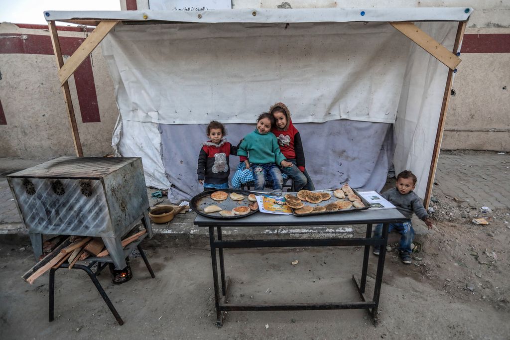 Beberapa anak Palestina duduk di dekat gerai roti di Deir al-Balah, kota Gaza, Minggu (3/3/2024).