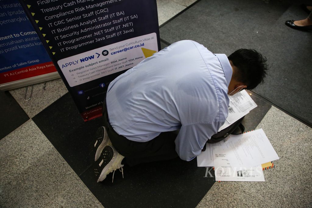 Seorang pencari kerja mempersiapkan berkas lamaran kerja di lantai tanpa mengindahkan kondisi di sekitarnya. 