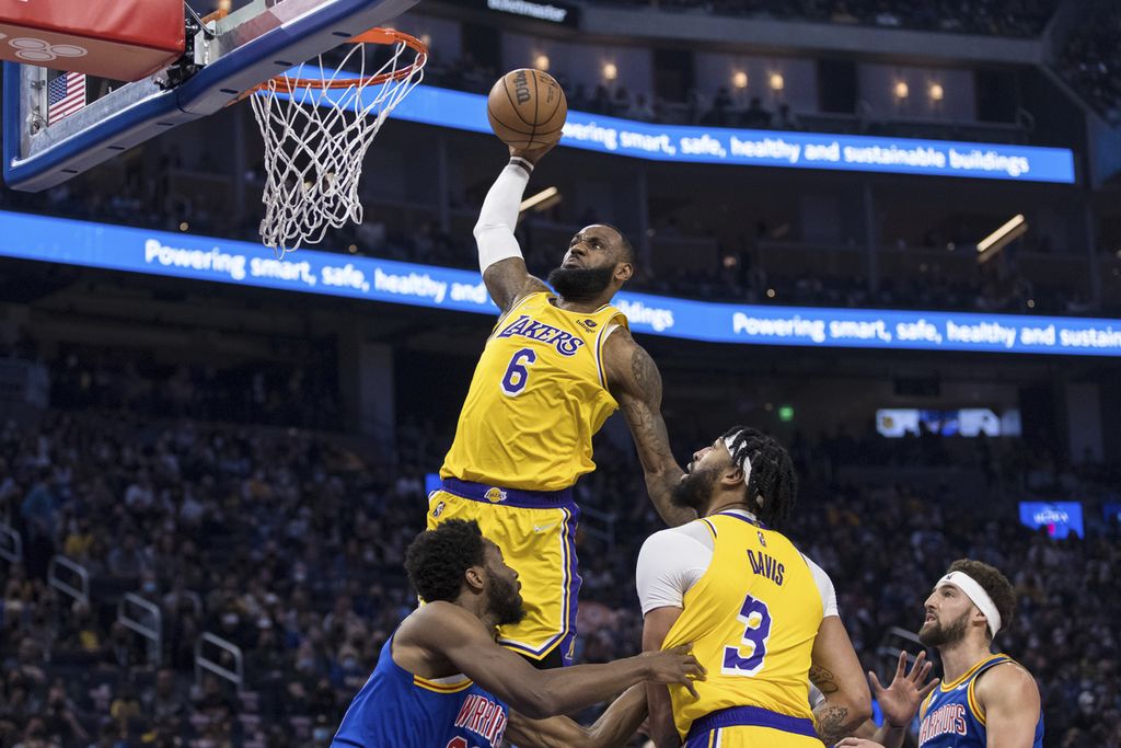 Bintang Los Angeles Lakers, LeBron James (atas), melakukan <i>dunk</i> saat melawan Golden State Warriors pada laga NBA di San Francisco, Minggu (13/2/2022) pagi WIB.