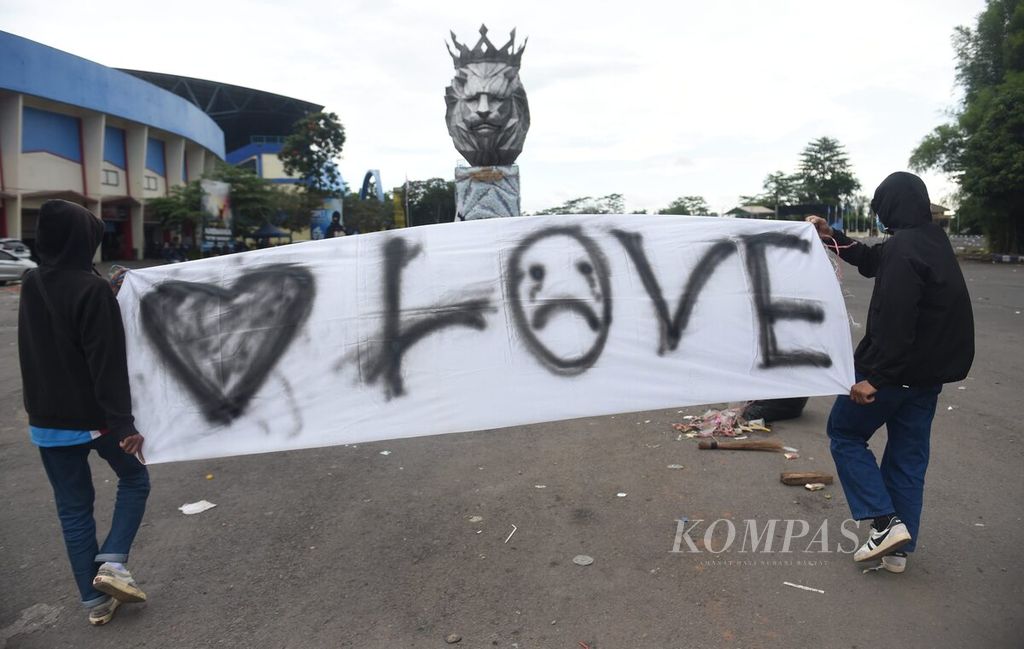 Aremania membawa spanduk bagi korban meninggal akibat kerusuhan untuk diletakkan di patung Singo Tegar yang berada di kompleks Stadion Kanjuruhan, Kabupaten Malang, Jawa Timur, Minggu (2/20/2022). 