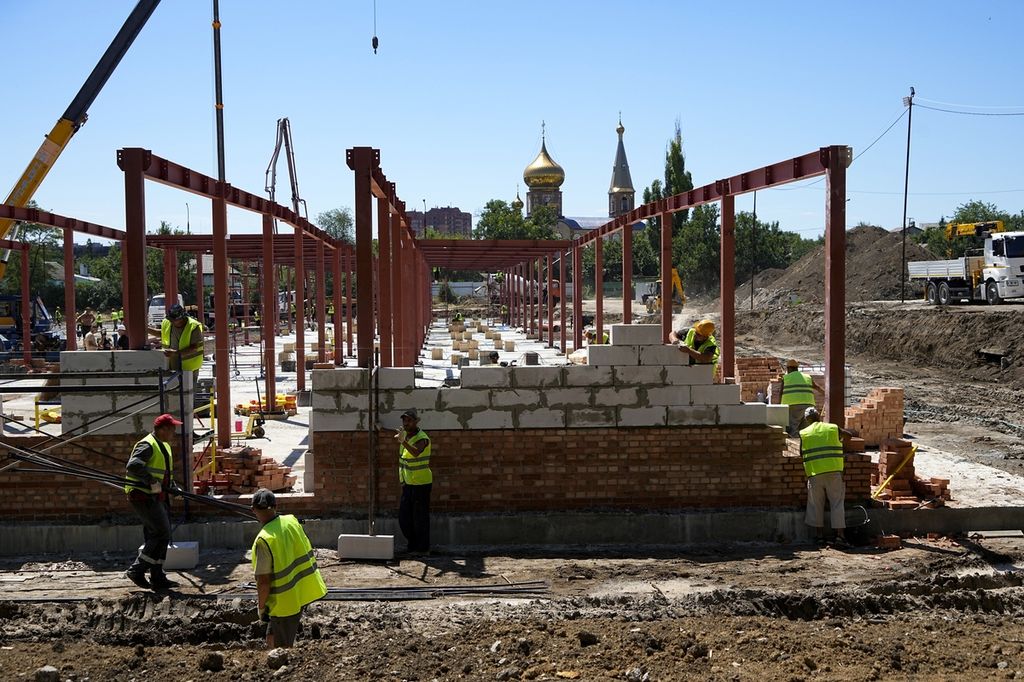 Construction workers work on the site of the new municipal medical center in Mariupol with an Orthodox church in the background, on the territory which is under the Government of the Donetsk People's Republic control, eastern Ukraine, Wednesday, July 13, 2022. This photo was taken during a trip organized by the Russian Ministry of Defense. 