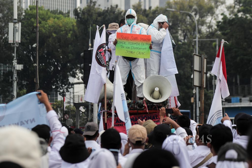 Peserta aksi yang menggunakan alat pelindung diri (APD) membawa poster berisi tuntutan saat aksi di kawasan Patung Kuda Arjuna Wiwaha, Jakarta, Senin (7/8/2023). 