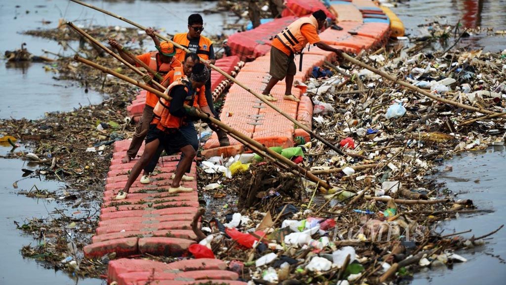 Petugas berusaha mendorong sampah ke pinggir sungai untuk selanjutnya diangkut ke darat menggunakan alat berat di Kanal Barat, Tanah Abang, Jakarta, Selasa (4/12/2018). Sebagian sampah yang tersangkut merupakan sampah rumah tangga, seperti plastik dan <i>styrofoam</i>.