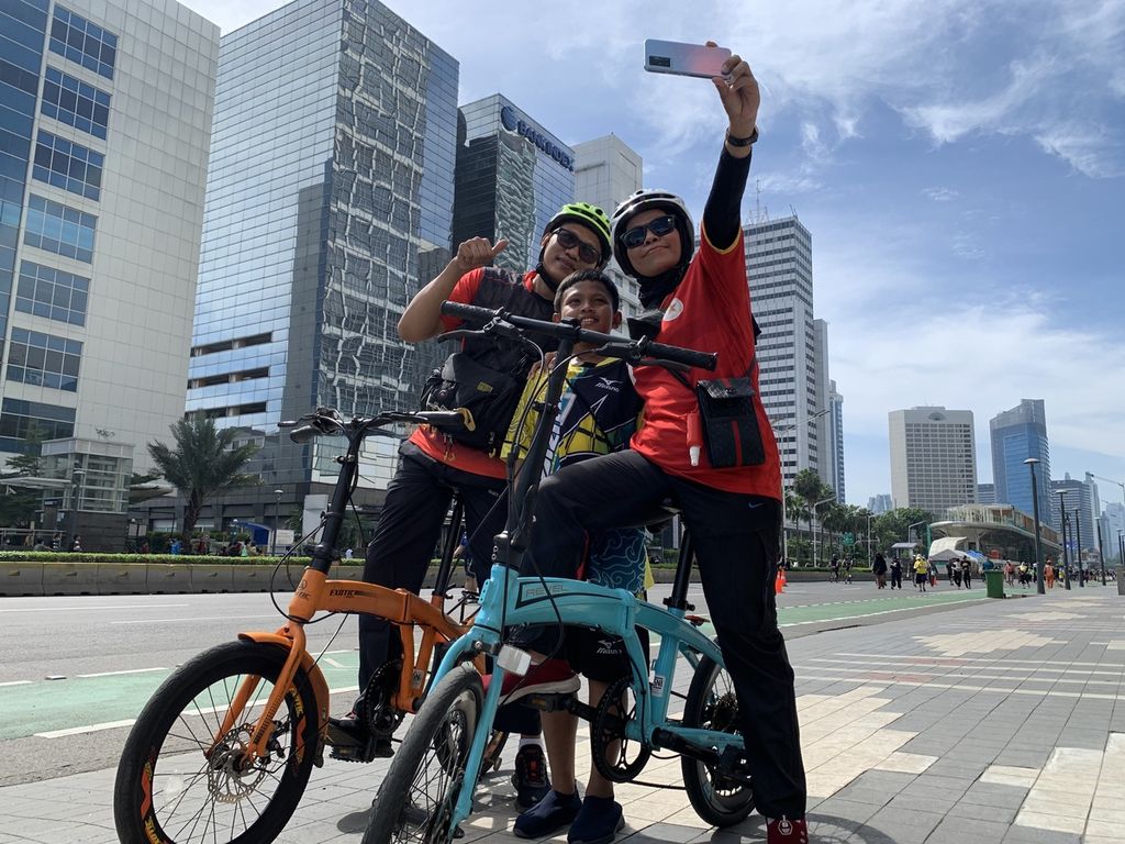 Fitri (34), Fadil (9), dan Sarizal (36), sedang melakukan swafoto di kawasan bebas kendaraan, dekat halte Transjakarta, Bundaran Hotel Indonesia (HI), Jakarta, Minggu (30/10/2022). Keluarga kecil itu memilih bersepeda di kawasan bebas kendaraan ketimbang jalan-jalan ke pusat perbelanjaan.