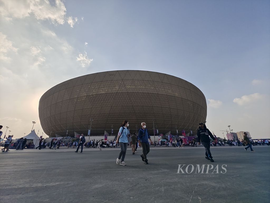 Suporter berjalan dengan latar Stadion Lusail jelang laga final Piala Dunia, Minggu (18/12/2022). Stadion Lusail adalah stadion terbesar di Qatar.