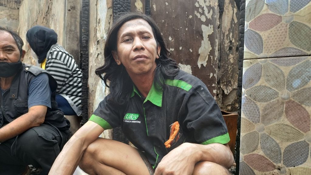 Tedi (43) tengah beristirahat seusai membersihkan rumahnya yang hangus terbakar di Kelurahan Kalianyar, Kecamatan Tambora, Jakarta Barat, Sabtu (31/12/2022).