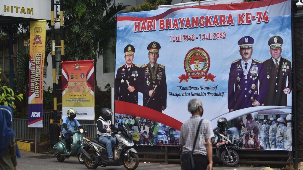 Warga melintas di depan baliho peringatan Hari Bhayangkara Ke-74 di pintu keluar Polda Metro Jaya, Jakarta, Selasa (30/6/2020). 