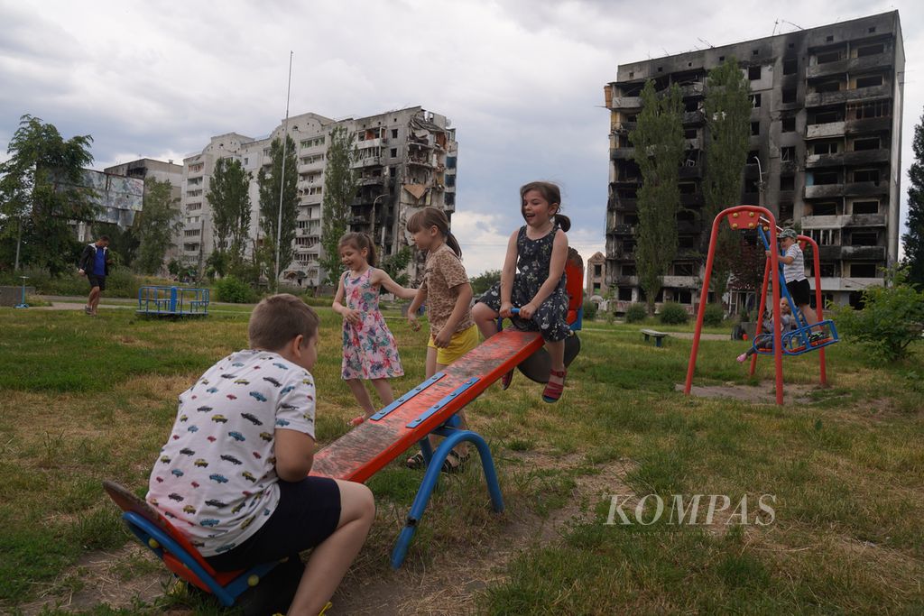 Anak-anak bermain di lapangan seberang sebuah apartemen yang hancur dihantam rudal Rusia di Borodyanka, Provinsi Kyiv, Ukraina, Jumat (17/6/2022). Banyak bangunan di Borodyanka yang luluh lantak akibat serangan Rusia. Kawasan ini sempat diduduki Rusia pada bulan pertama perang terjadi. 