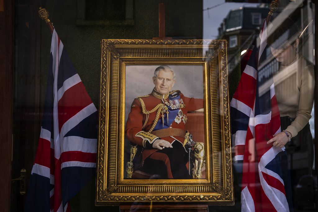 Seorang pegawai menata dekorasi jendela sebuah toko yang dihiasi lukisan Raja Inggris Charles III di London, Kamis (4/5/2023). 