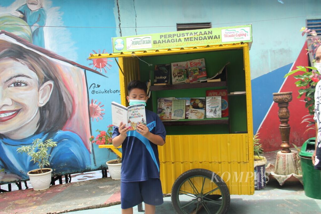 Seorang anak sedang membaca di gerobak baca Rumah Kreatif, Kampung Mendawai, Kota Pontianak, Kalimantan Barat, Sabtu (3/4/2021).