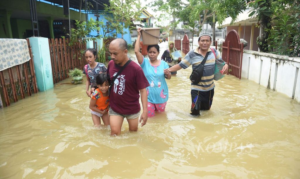 Secara bersama-sama warga melintasi banjir yang berarus di di Jalan Kenari, Kecamatan Sampang, Kabupaten Sampang, Jawa Timur, Senin (2/1/2023). Luapan Sungai Kemuning sejak Minggu (1/1/2023) menyebabkan beberapa kawasan di Kabupaten Sampang terendam banjir. Ketinggian banjir hingga 2 meter di beberapa titik. 