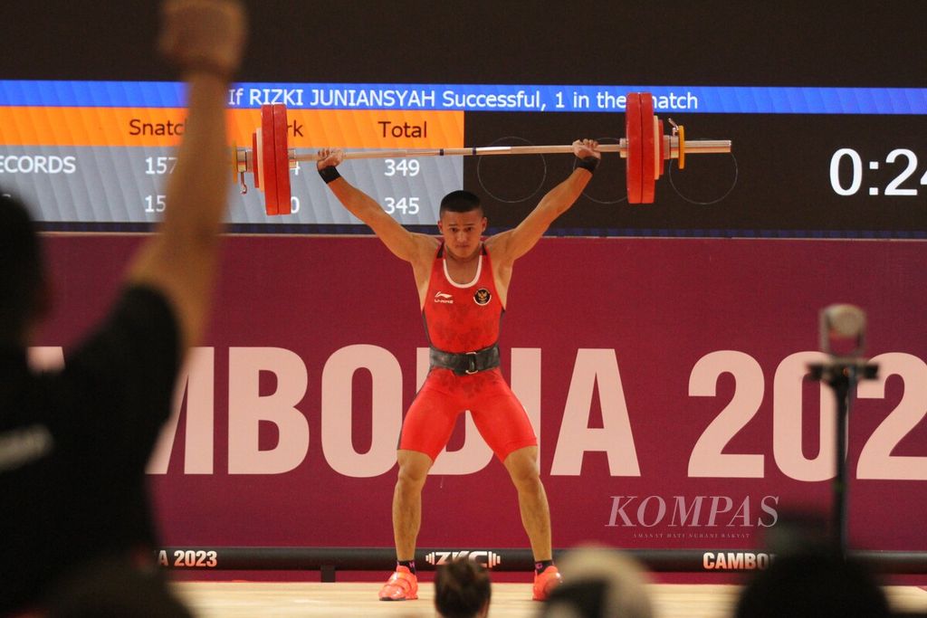 Rizki Juniansyah, lifter muda Indonesia, mengangkat pelat-pelat besi seusai memecahkan rekor dengan total angkatan 347 kilogram (<i>snatch</i> 156 kg dan <i>clean and jerk</i> 347 kg) di cabang angkat besi kelas putra 73 kilogram di National Olympic Stadium, Kamboja, Minggu (14/5/2023). 
