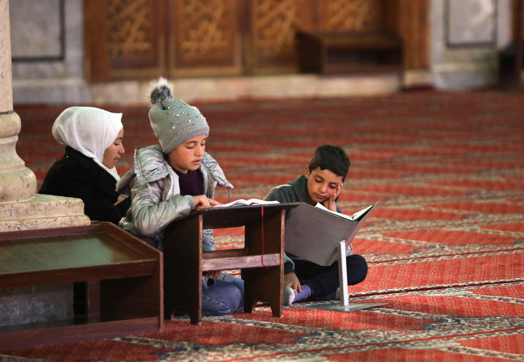 Anak-anak membaca Al Quran di Masjid Umayyah setelah berbuka puasa pada hari pertama bulan suci Ramadhan, di Damaskus, Suriah, Selasa (13/4/2021). 