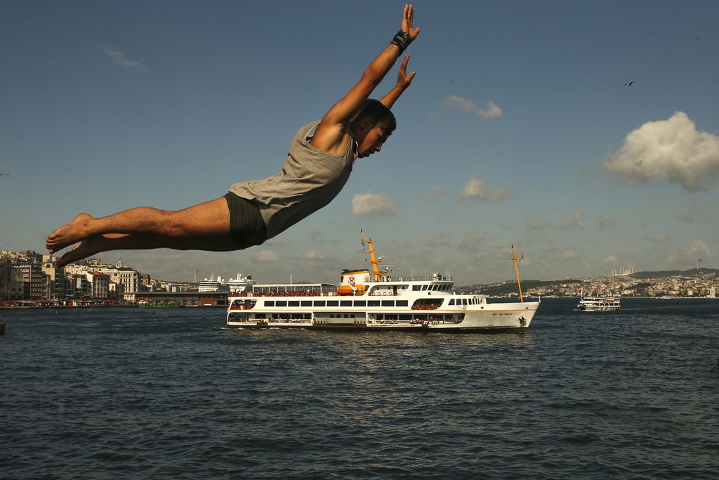 Seorang remaja melompat dari Jembatan Galata ke Golden Horn yang mengarah ke Selat Bosphorus, selat pemisah antara Eropa dan Asia, di Istanbul, Turki, 9 Agustus 2022. 