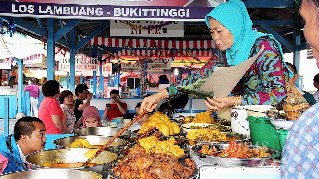 Ernida, yang akrab dipanggil Uni (kakak) Er, sedang mengambil lauk dan sayuran di kedai nasi kapau miliknya di Los Lambuang, Pasar Bawah, Kota Bukittinggi, Sumatera Barat. Nasi kapau dikenal bercita rasa enak dan unik dibandingkan dengan nasi padang umumnya.