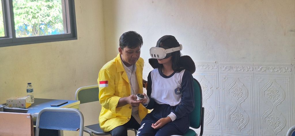 Siswa SMPN 8 Depok mencoba perangkat <i>virtual reality</i> didampingi anggota tim pengabdian masyarakat Fakultas Ilmu Keperawatan UI.