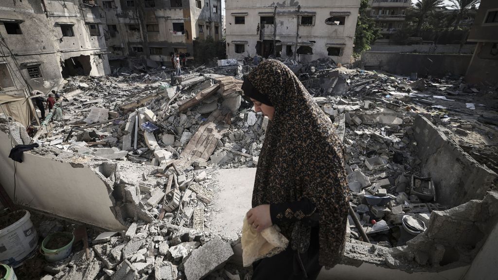 Perempuan Palestina melewati puing-puing bangunan di depan rumahnya di kota Gaza, Palestina, yang luluh lantak karena serangan Israle, Senin (8/8/2022). Setelah tiga hari konflik, Israel dan Palestina menyepakati gencatan senjata.