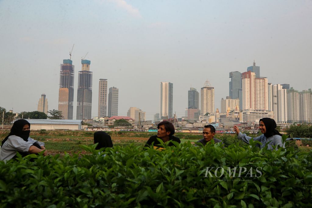 Warga mengobrol di kawasan Petamburan dengan latar belakang gedung-gedung tinggi di Tanah Abang, Jakarta, Rabu (5/7/2023). 