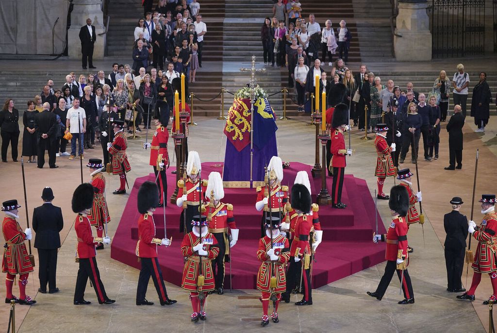 Warga yang hendak memberi penghormatan terakhir pada mendiang Ratu Elizabeth berhenti sejenak, memperhatikan prosesi pergantian penjaga yang akan berdiri di sekitar peti jenazah di Aula Westminster, London, Rabu (14/9/2022). 