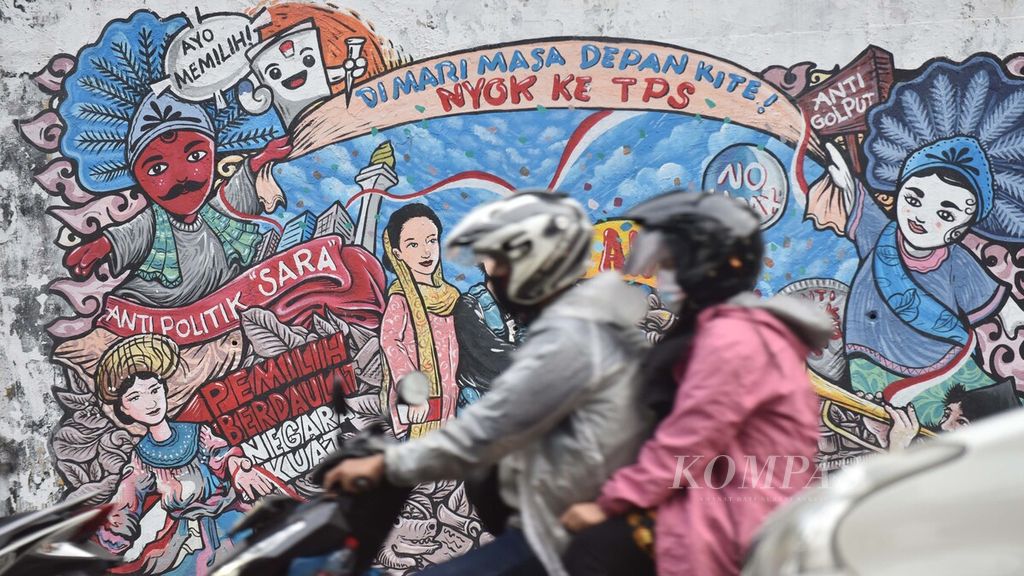 Pengendara sepeda motor melintasi mural kampanye anti-SARA dalam pemilihan umum yang tergambar di dinding Jalan Dukuh Atas, Jakarta, Jumat (19/6/2020). 