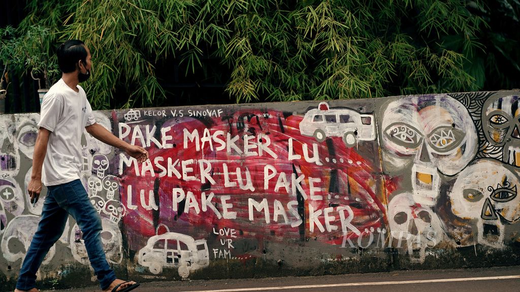 Warga melintasi grafiti untuk memakai masker di Duren Sawit, Jakarta Timur, Selasa (10/8/2021). Seiring perpanjangan PPKM level 4 seminggu ke depan, diharapkan angka kasus akan menurun lebih signifikan. Bed occupancy rate (BOR) di Jakarta turun terus sampai 39 persen di 140 RS rujukan Covid-19, kemudian BOR ICU 65 persen. KOMPAS/AGUS SUSANTO (AGS) 10-8-2021