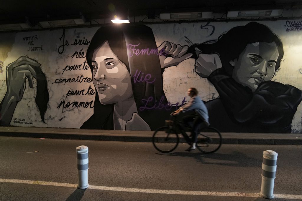 Seorang wanita mengendarai sepeda di depan mural yang menggambarkan wanita tengah memotong rambut mereka, di sebuah terowongan di Paris, Perancis, Rabu (5/10/2022). Mural itu menunjukkan dukungan bagi pengunjuk rasa Iran.