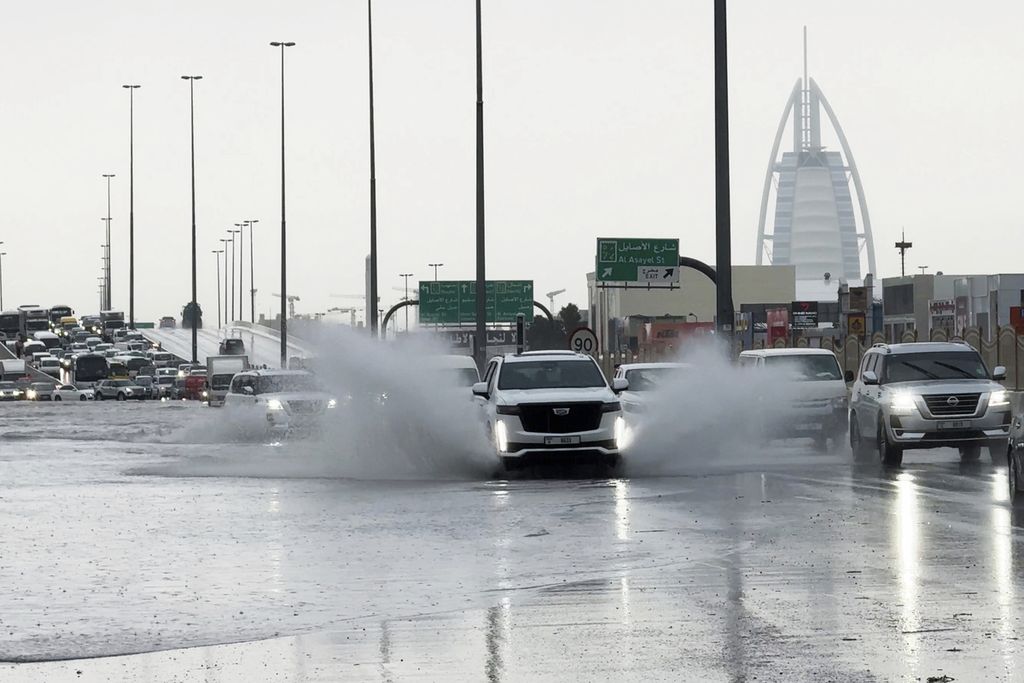 An SUV drives through a puddle on a road with the luxury Burj Al Arab hotel in the background in Dubai, United Arab Emirates, on Tuesday (16/4/2024). Heavy rain hit the UAE that day, flooding some of the main highways and leaving stranded vehicles on the roads crossing Dubai.