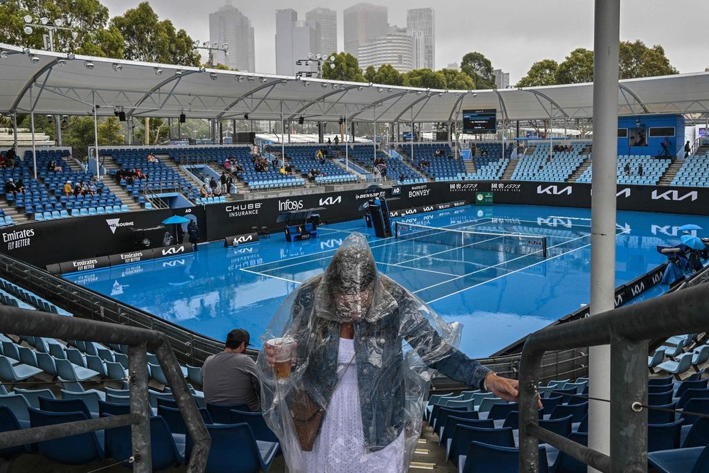 Penonton mengenakan jas hujan dengan lapangan yang basah akibat hujan pada hari ketiga turnamen tenis Grand Slam Australia Terbuka di Melbourne Park, Rabu (18/1/2023). Hujan membuat banyak pertandingan tertunda dan petenis menunggu sangat lama untuk bermain.