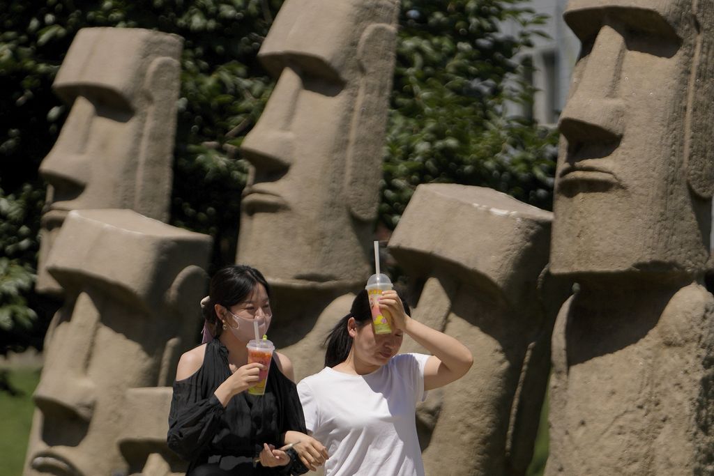 Dua perempuan coba mengurangi panas yang menyengat dengan menempelkan minuman dingin ke kepalanya saat berjalan di bawah terik matahari di Beijing, China, Rabu (21/6/2023). Sepekan terakhir, Beijing dan beberapa kota di utara China dilanda gelombang panas yang menyengat. 