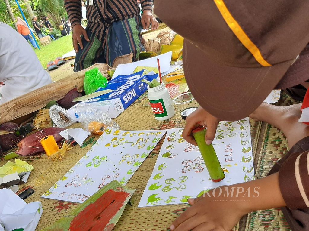 Seorang anak menggunakan pelepah pisang untuk menggoreskan cat warna di kertas, Sabtu (21/5/2022).