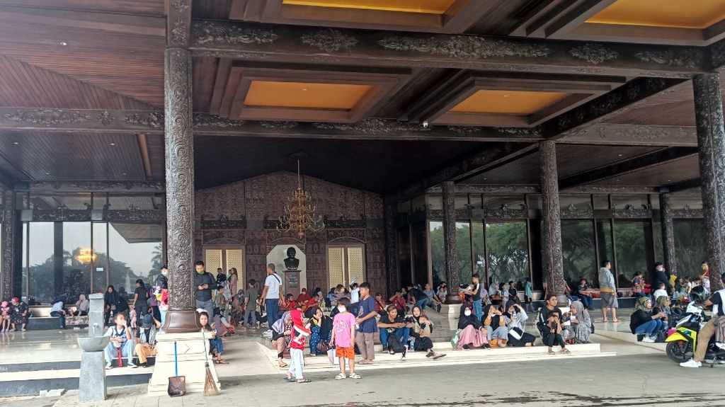 Pengunjung Taman Mini Indonesia Indah (TMII) yang sedang berteduh akibat hujan deras di Gedung Sasono Adiguno TMII, Jakarta Timur, Senin (26/12/2022). Hujan deras yang mengguyur kawasan TMII pada pagi dan sore hari tidak menyurutkan niat wisatawan untuk tetap berkunjung.