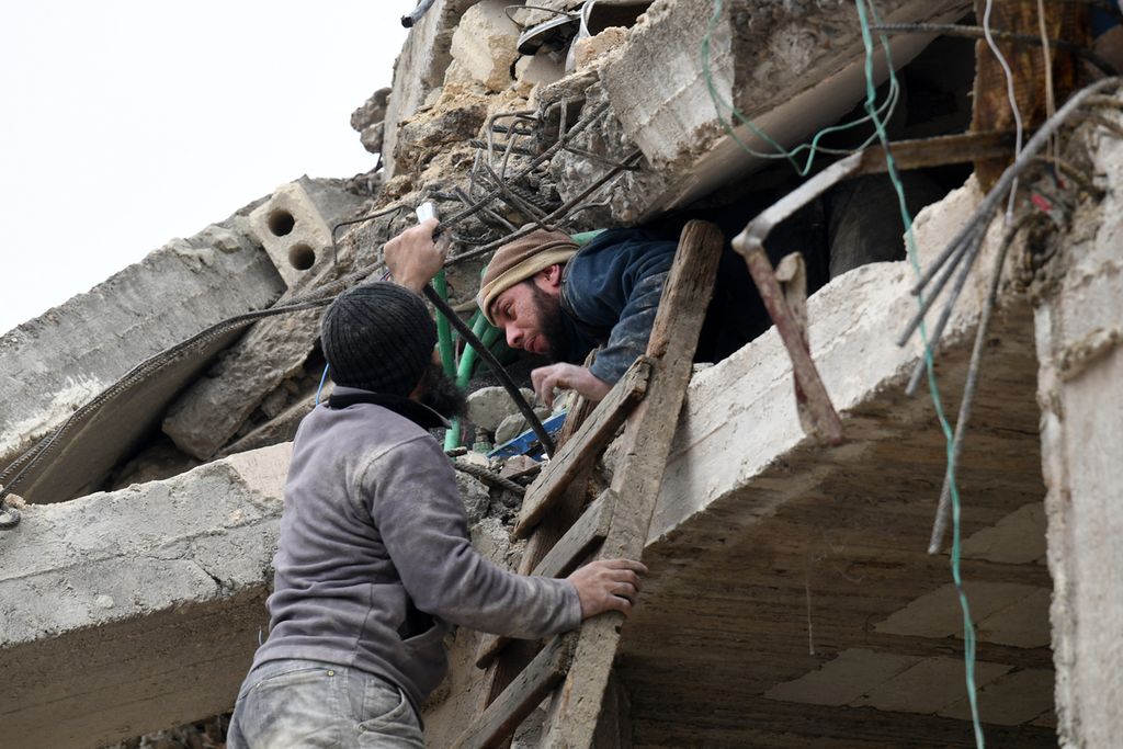 Seorang warga yang terjebak di bawah reruntuhan gedung di Kota Jandaris, Suriah, coba diselamatkan oleh beberapa warga, usai kota itu dilanda gempa, Senin (6/2/2023). (Photo by Rami al SAYED / AFP)