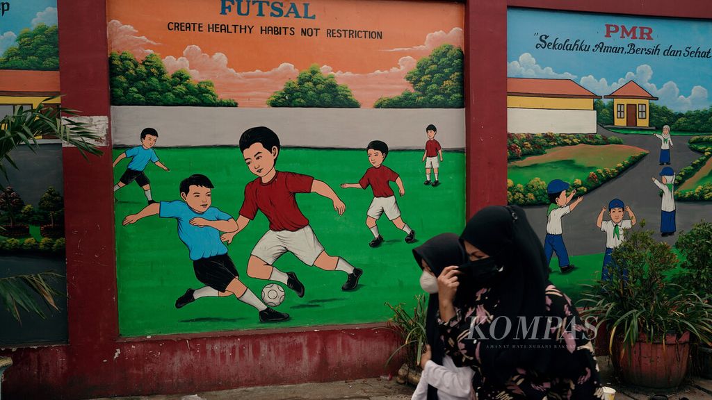 Warga melintasi mural olahraga anak yang menghiasi sebuah gedung sekolah dasar di Sukapura, Cilincing, Jakarta Utara, Senin (14/3/2022).