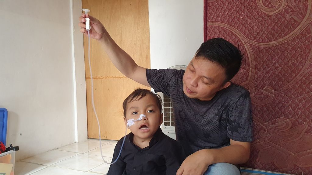 Tay David Sulu (36) memangku anaknya, Alvaro (4), yang masih berjuang untuk sembuh setelah mengalami gangguan ginjal akut progresif atipikal (GGAPA) saat ditemui di rumah kontrakannya di Jalan Masjid nomor 110 RT 009 RW 008, Lenteng Agung, Jagakarsa, Jakarta Selatan, Minggu (9/7/2023).